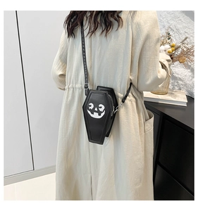 Black coffin-shaped crossbody bag with white pumpkin face print worn by a model