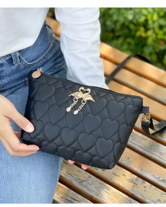 Close-up of heart-quilted black shoulder bag with gold double heron hardware on a model