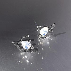 Detailed view of silver wing ear clips with shimmering moonstone on metallic background