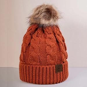Detail of cable knit beanie with faux fur pom pom and leather logo patch in orange