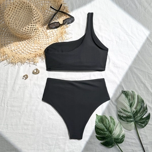 Detail view of black one-shoulder bikini with high waisted bottoms and vacation accessories