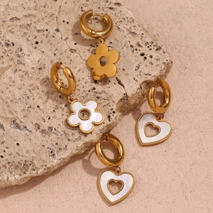 Macro view of gold flower and heart charms with white mother of pearl inlay on hoop earrings
