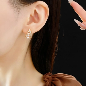 Close-up of elegant gold pearl earrings with a triangle zircon frame on model's ear