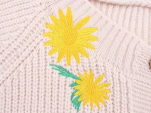 Close-up of sunflower embroidery and ribbed texture on the beige knit cardigan