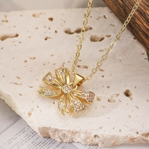 Sparkling zircon bow pendant necklace in gold finish on a natural stone background