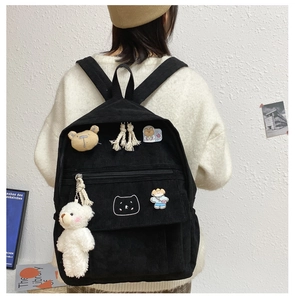 Detalle de mochila de pana negra con parches de oso y colgante de peluche blanco suave