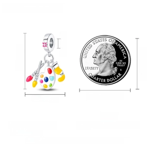 Detail of silver artist palette charm with enamel brushes beside a quarter coin