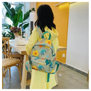 Close-up of green kids backpack with floral print and round mini pouch on a back