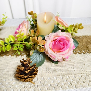 Close-up of pink artificial roses and pine cones wreath with glowing LED candle