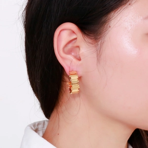 Vue détaillée de boucles d'oreilles dorées à texture étagée portées par un mannequin