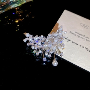 Detailed view of silver zircon brooch with elegant white pearls on a dark reflective surface