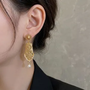 Elegant gold hollow petal earrings with white pearls and teardrop pendant on model