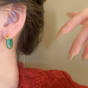 Macro detail of U-shaped emerald green zircon earrings with vintage gold plating