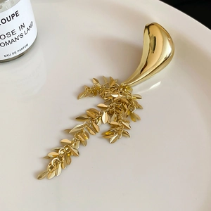 Elegant gold metal brooch with geometric leaf tassels on white background plate