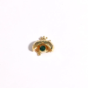 Macro detail of a 3D ladybug pendant in gold finish with a green center gemstone