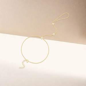 Detail of a golden slave bracelet featuring delicate white flowers and dainty chain links