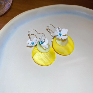 Detail of white flower earrings with yellow round pendants on a ceramic plate