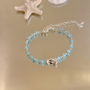 Detailansicht des silbernen Delfinanhängers an einem blauem Perlenarmband im Seestil