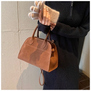 Detail of brown suede tote bag with round handle and shoulder strap held by model