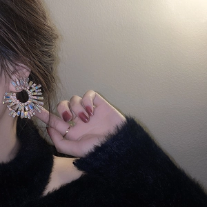 Detail showing oversized iridescent crystal earring worn by model on black sweater