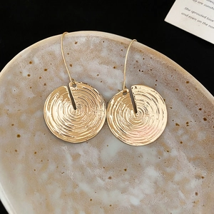 Macro detail of gold round earrings with concentric texture on a ceramic dish