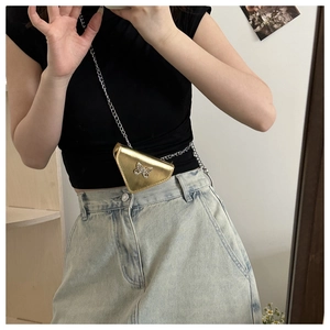 Detail of a triangle mini bag with gold finish, rhinestone bow, and silver chain strap