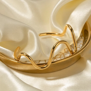 Detailed view of an 18k gold-plated stainless steel wavy cuff bracelet on a satin fabric