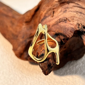 Irregular geometric gold titanium steel open ring on a textured dark wood block