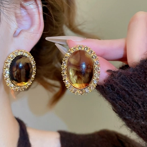 Detailed view of amber resin oval earrings with sparkling crystal halo on golden metal