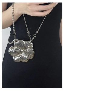 Detail of silver metallic flower-shaped crossbody bag with bead chain on model