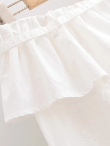 Détail de pantalon blanc avec taille à volants et boucle de ceinture assortie