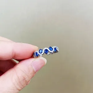 Fashionable silver ring featuring five oval blue gemstones and wavy diamond accents