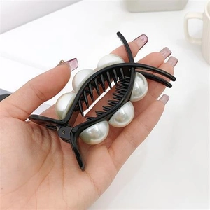 Détail d'une pince à cheveux noire ornée de huit perles blanches élégantes tenue en main