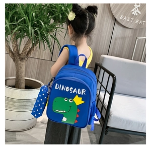 Rear view of a blue kids dinosaur backpack worn by a model, including a star-print pencil case