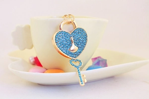 Detail of gold heart lock keychain with blue rhinestones on a decorative ceramic dish