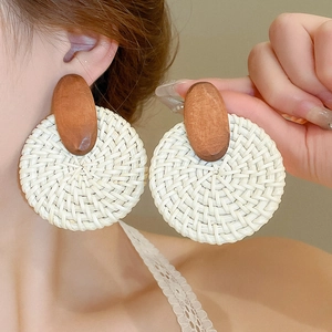 Détail de grandes boucles d'oreilles bohèmes en raphia avec bois et disque tissé blanc