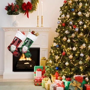 Detail of red and green plaid Christmas stockings with gnome motifs hanging on a fireplace