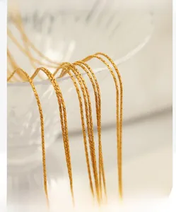Detailed macro view of layered golden snake chains hanging on textured glass