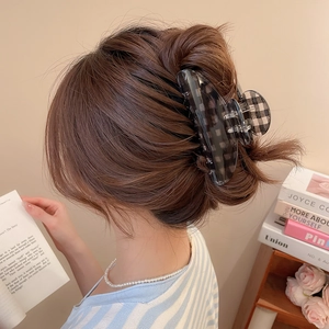 Close-up of a large checkered acrylic hair claw clip styling a low bun in thick hair