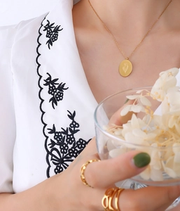 Macro detail of gold floral engraved oval pendant and multilayered stackable rings