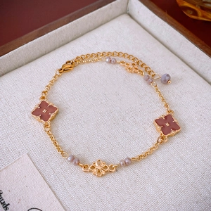 Bracciale dorato con quadrifogli terracotta e perline viola su sfondo di lino