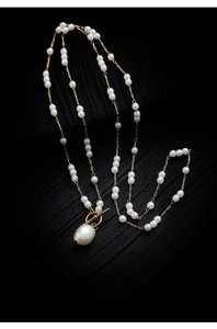Close-up of golden chain necklace featuring a baroque pearl pendant and OT toggle clasp
