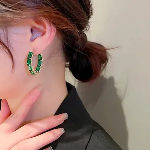 Golden C-shaped geometric hoop earrings with emerald green zircons on a female model