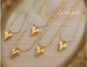 Detailed view of 5-piece 18K gold plated heart pendants on bead chains on wood