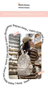 Close-up of white canvas backpack with strawberry print and fuzzy pom-pom charm