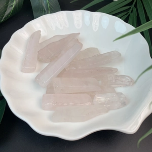 Close-up of raw natural rose crystal quartz columns in a white shell-shaped ceramic bowl