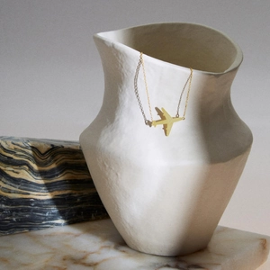 Détail artistique d'un collier avion doré drapé sur un vase en céramique blanche texturée