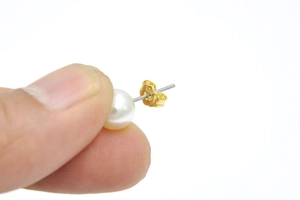 Close-up of a white pearl stud earring with a secure gold-plated butterfly back