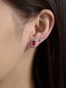 Detailed close-up of emerald-cut ruby earrings with halo diamonds worn on a model's ear