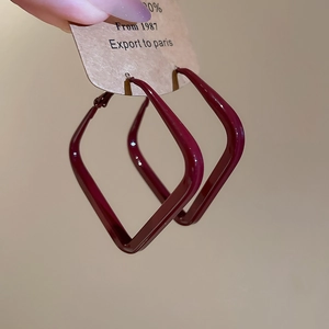 Close-up of burgundy square geometric earrings held on a kraft paper display card